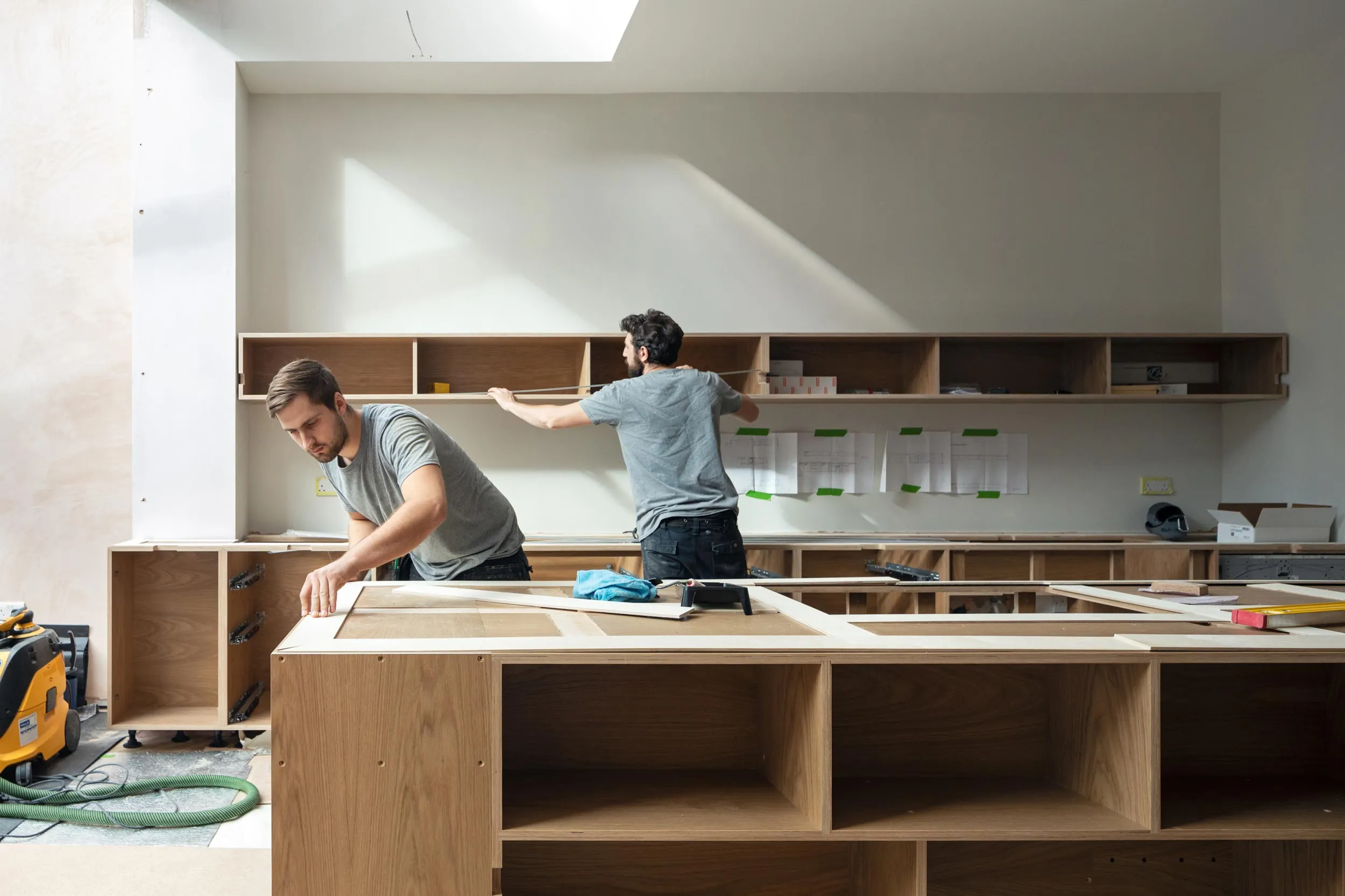 Uncommon Projects team installing bespoke oak-veneered plywood kitchen cabinetry on site