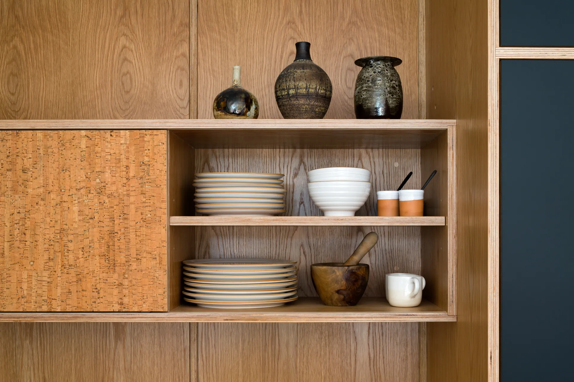 Open oak-veneered plywood kitchen shelving with cork sliding panel and stacked ceramics by Uncommon Projects