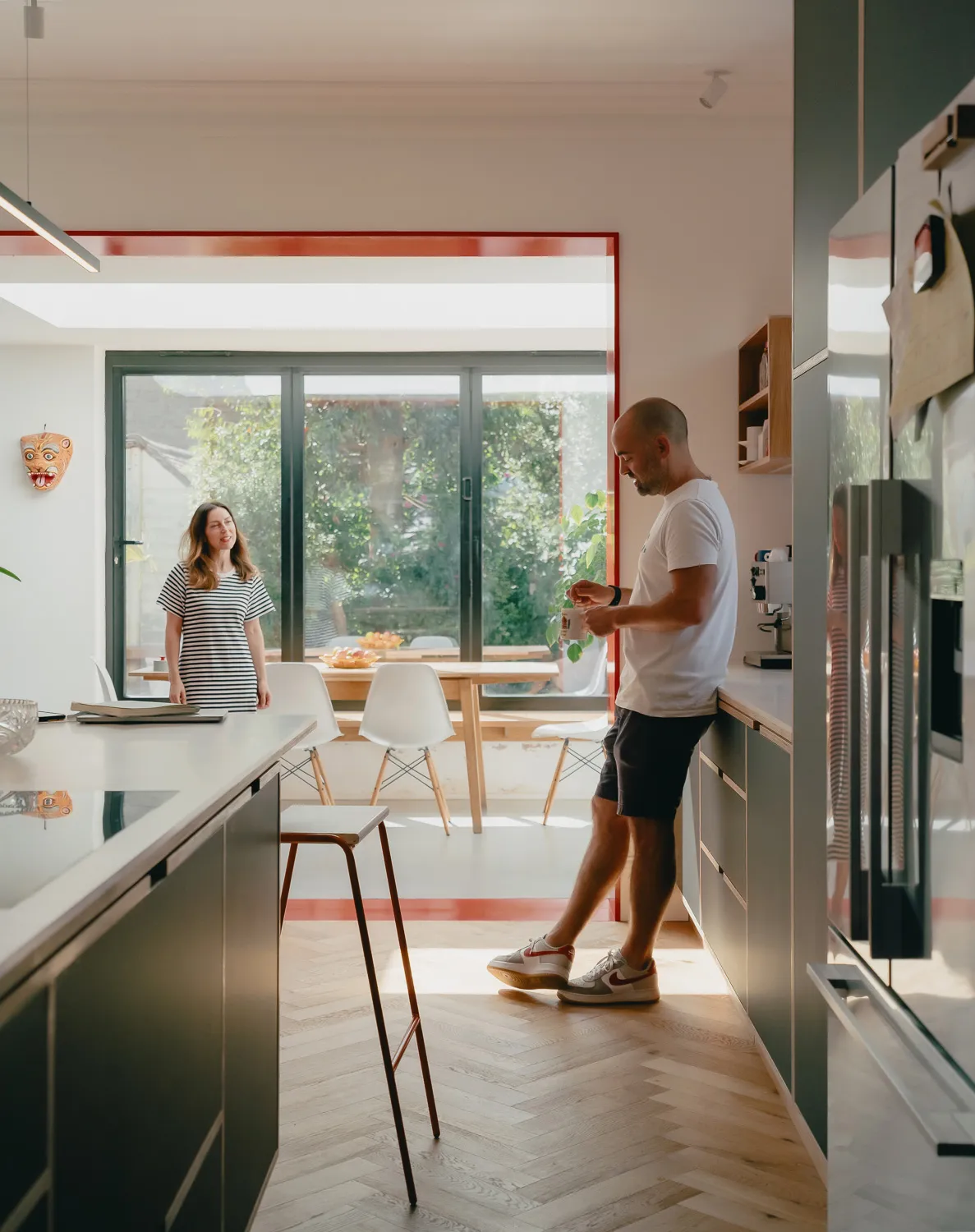 Family in bespoke Uncommon Projects kitchen with dark cabinetry, white island and herringbone oak floor