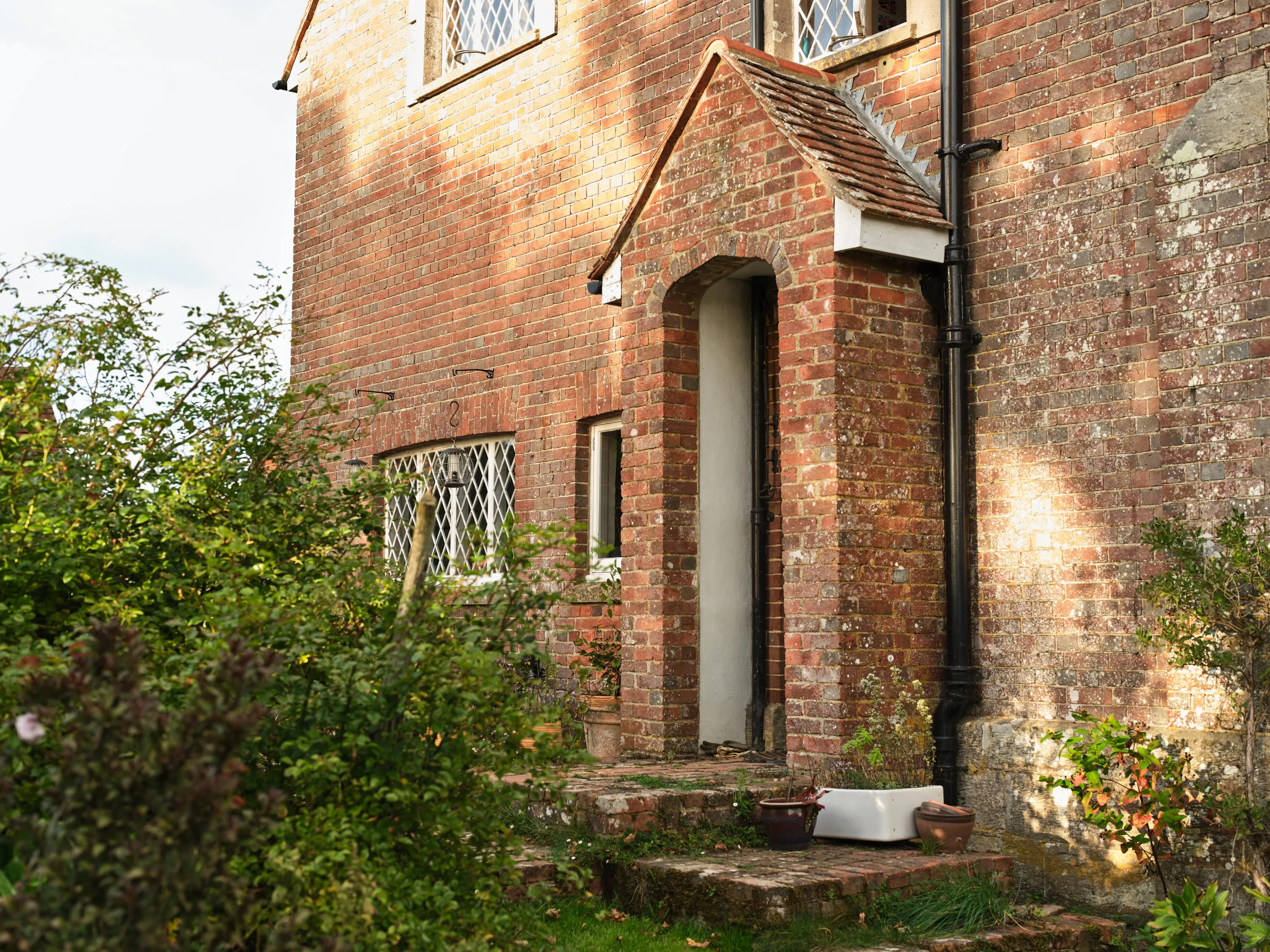 Brick house exterior with a small arched porch entrance and plants growing around a stone staircase.