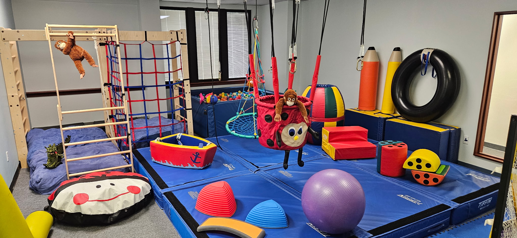 Indoor sensory playroom with climbing frame, ball pit, swings, soft shapes, and plush monkeys.