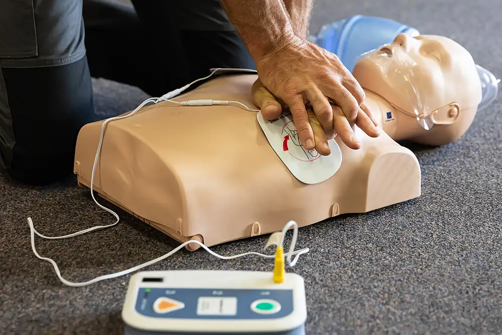 First aid course instructor demonstrating CPR with a resuscitator on a training dummy.