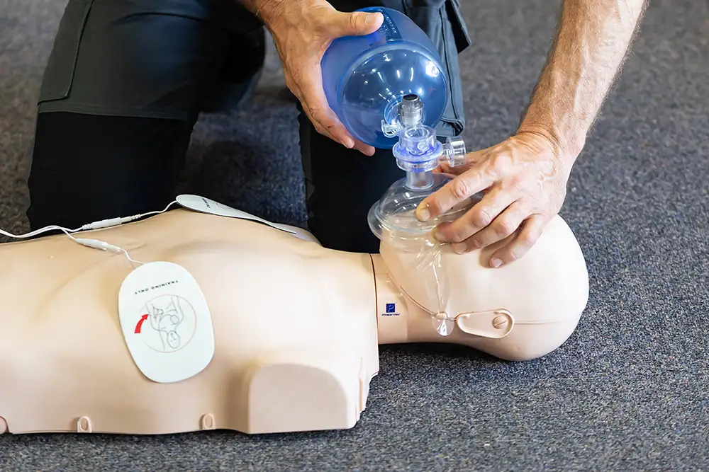 First aid course instructor demonstrating CPR with a resuscitator on a training dummy.