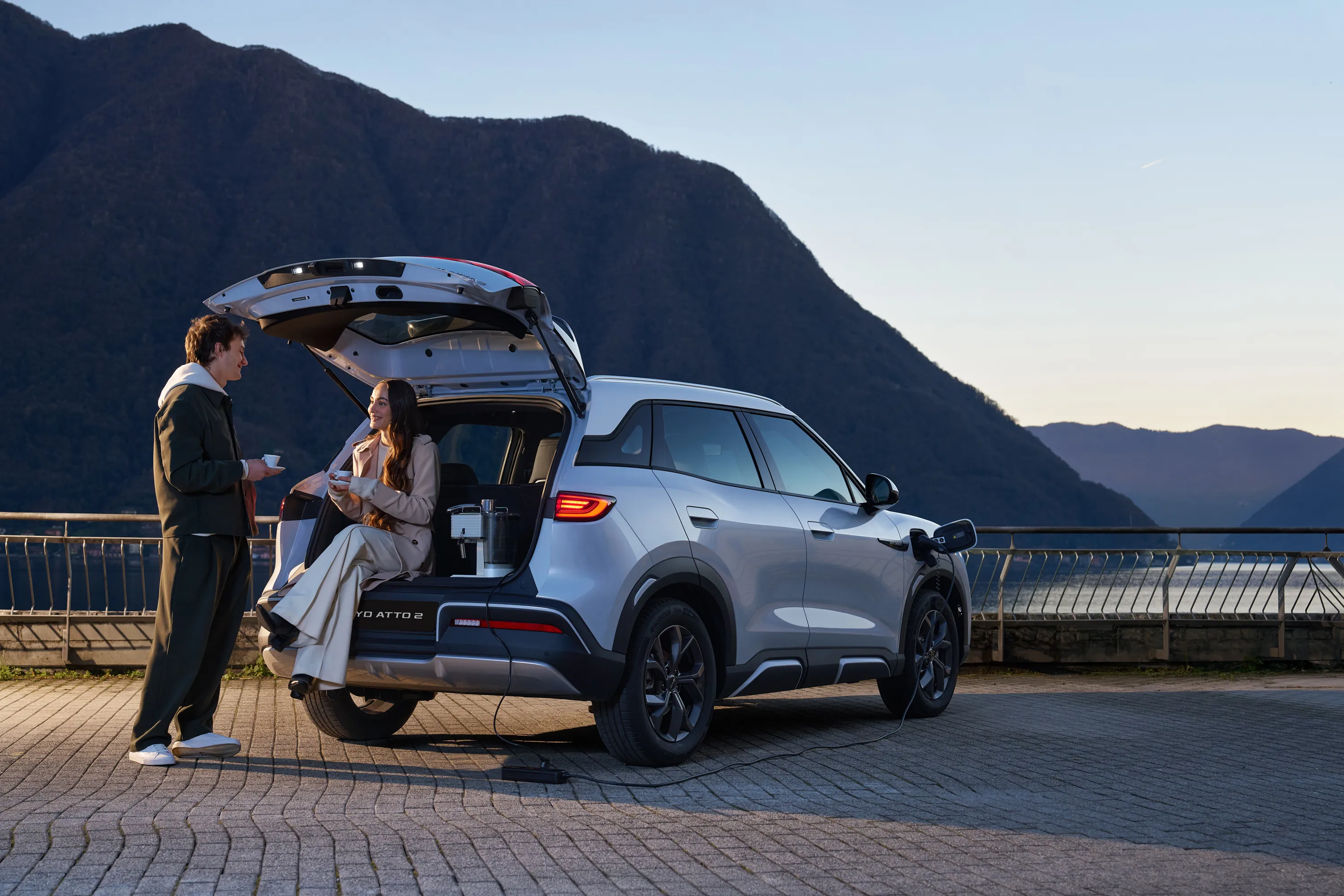 BYD ATTO 2 Außenansicht am See, zwei Personen sitzen am Kofferraum.