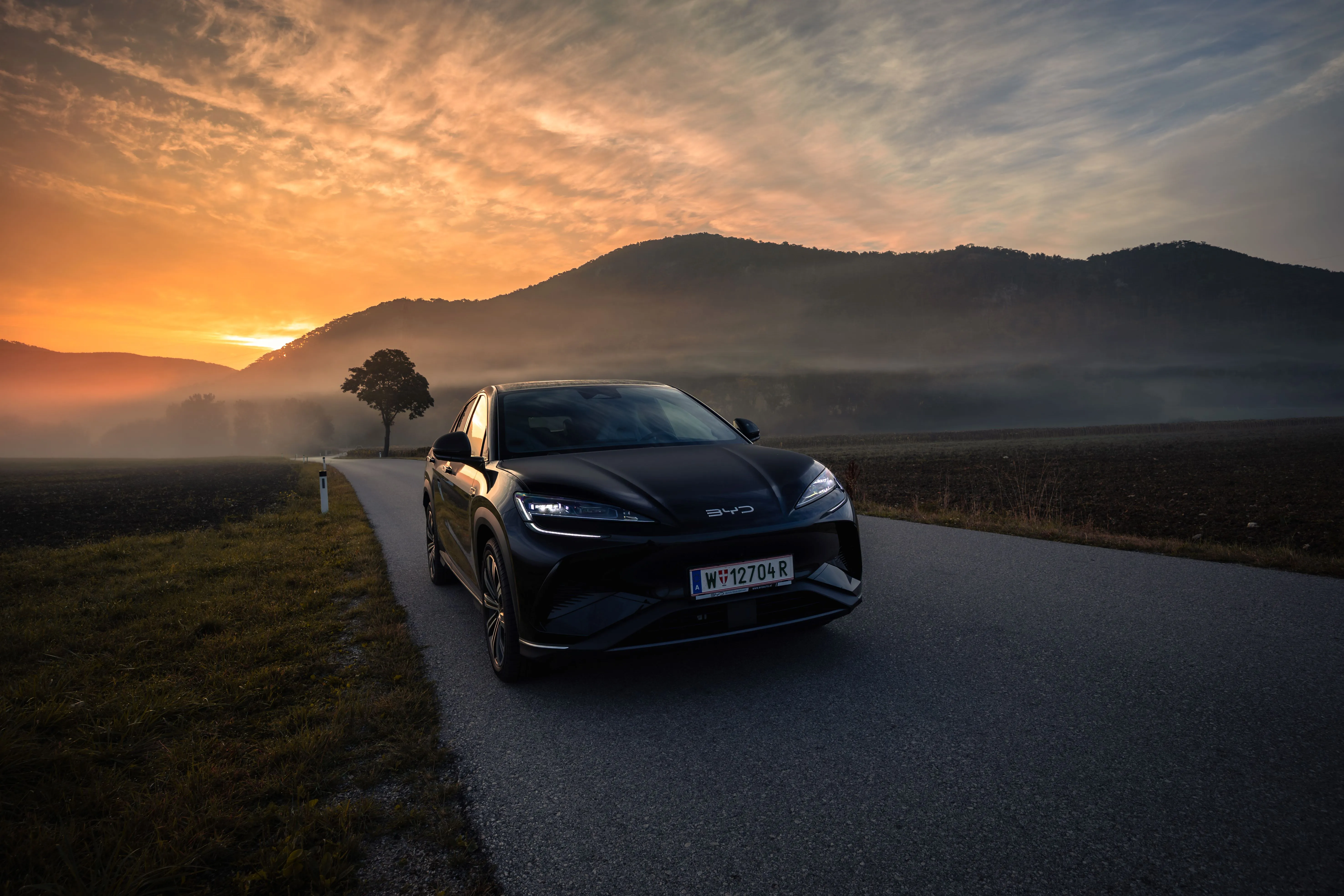 BYD SEALION 7 in blau steht vor einem Gebäude, eine Frau steht daneben und lächelt in die Kamera.