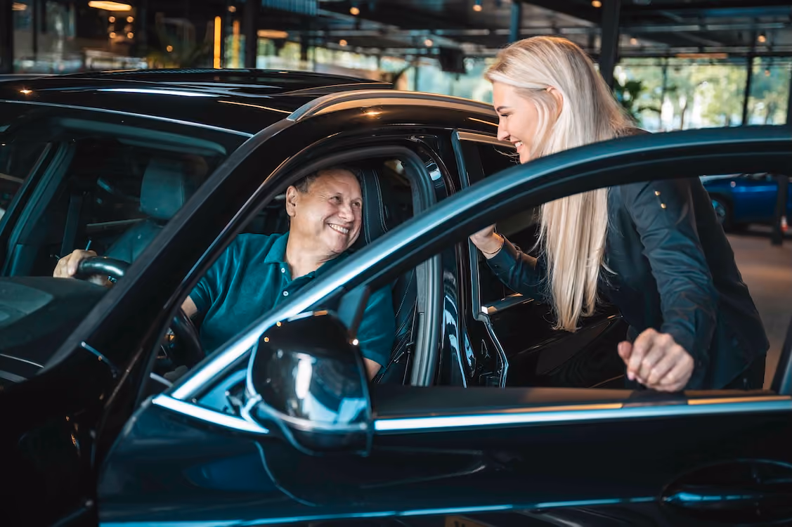 Klant zit in een auto klaar om weg te rijden en praat glimlachend met een medewerker van Vandaag Verpanden, die de deur openhoudt.