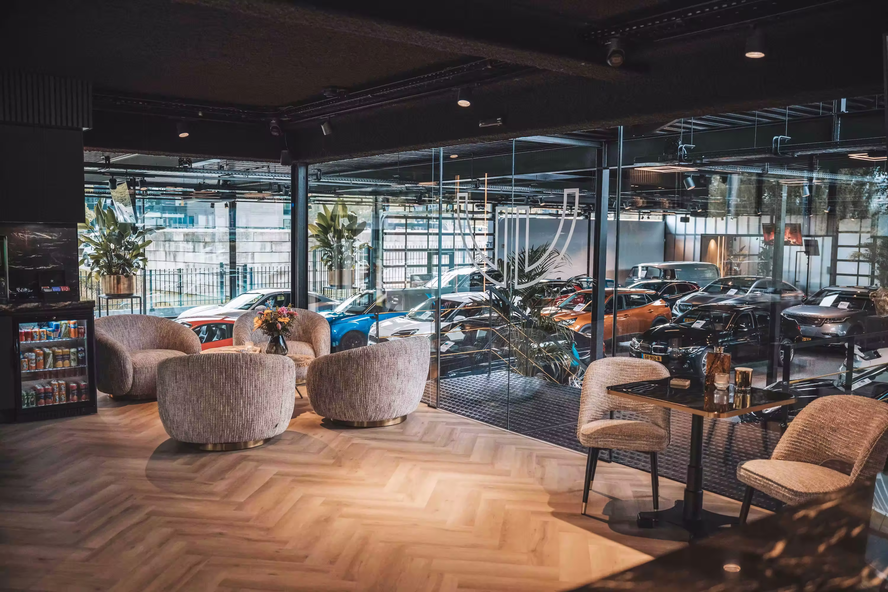 Wachtruimte van Vandaag Verpanden met loungestoelen, een houten visgraatvloer en zicht op de showroom met voertuigen op de achtergrond.