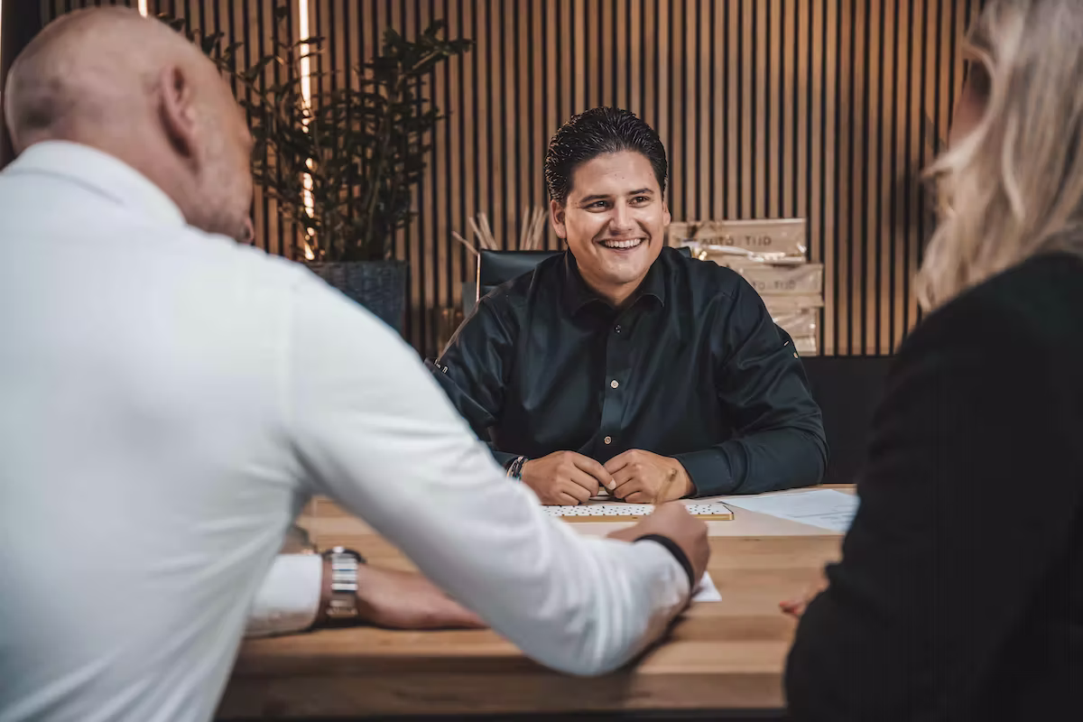 Twee klanten in gesprek met een medewerker van Vandaag Verpanden aan een houten tafel.