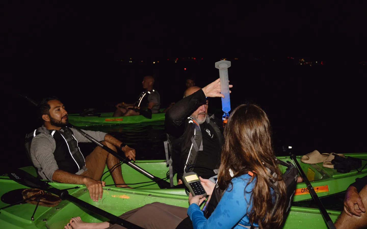 A group of people in a green kayak at night.