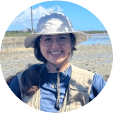 A woman wearing a hat and glasses on a beach.
