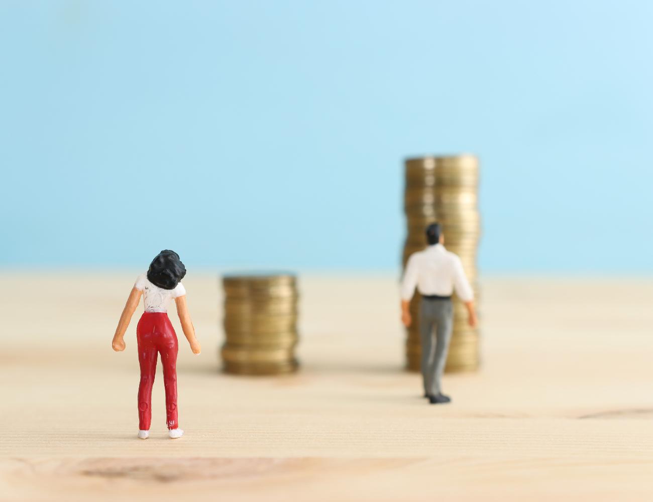 man and woman figurines. women is walking towards short stack of coins, man is walking towards bigger stack of coins