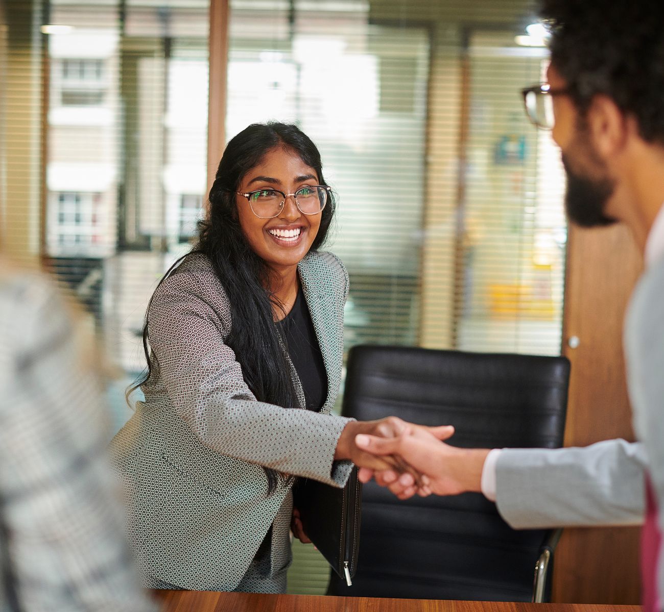 a smiling woman shakes hand with her new coworker in an office setting