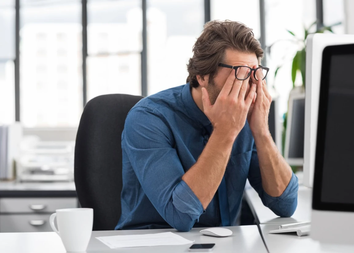 man rubbing his eyes in frustration with his work