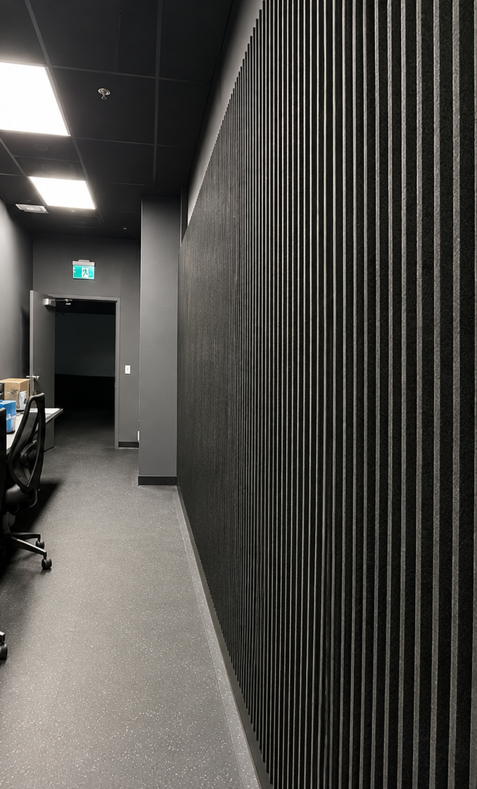 Floor-to-ceiling black acoustic slat wall in a dark Toronto office corridor