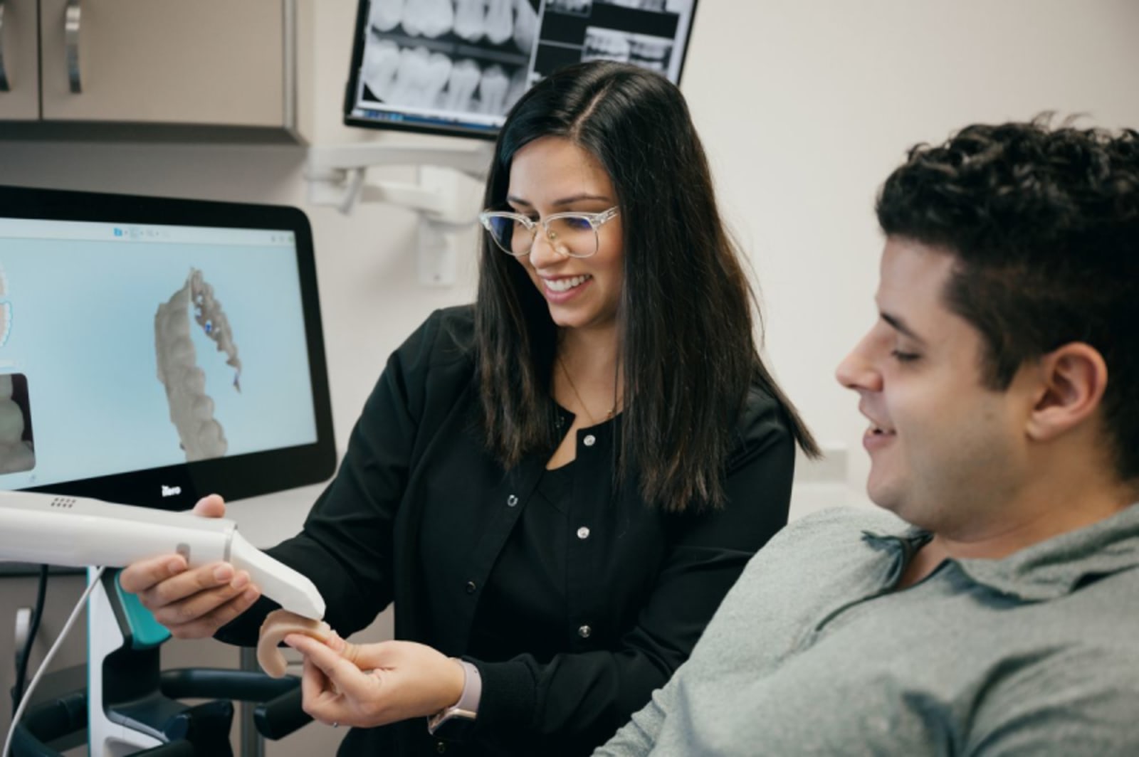 Female dentist showing dental bridge model to male patient in office treatment room