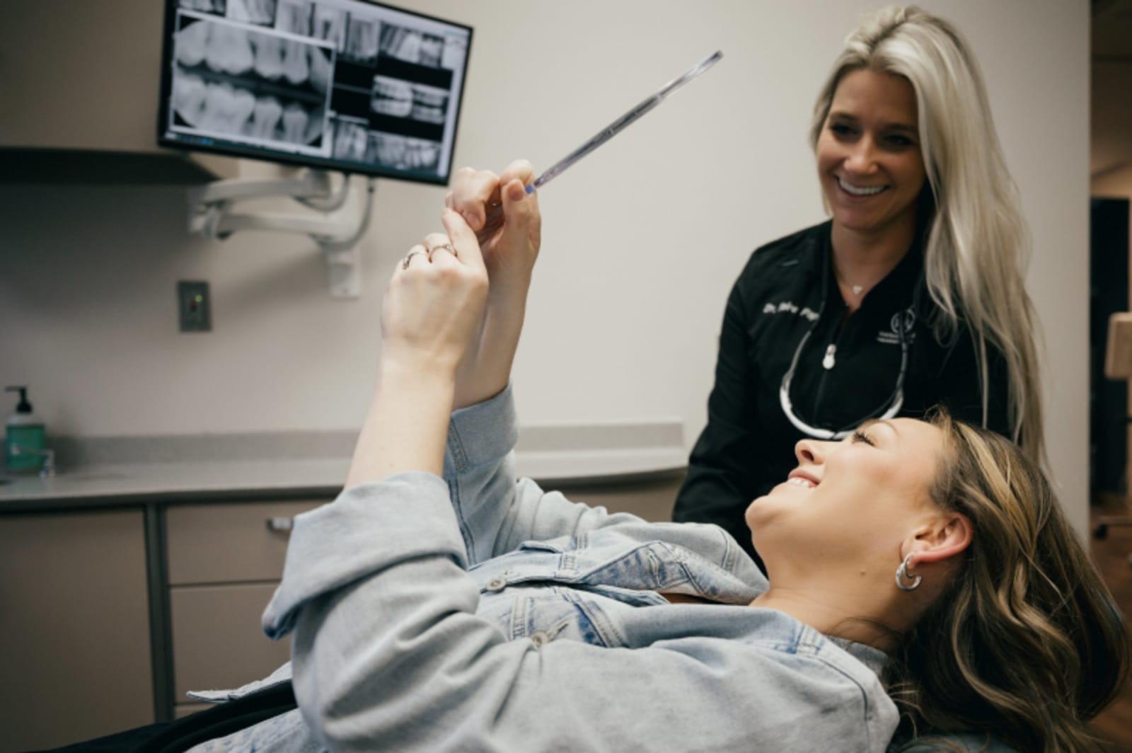 Female dentist discussing X-rays with male patient in dental office treatment room.