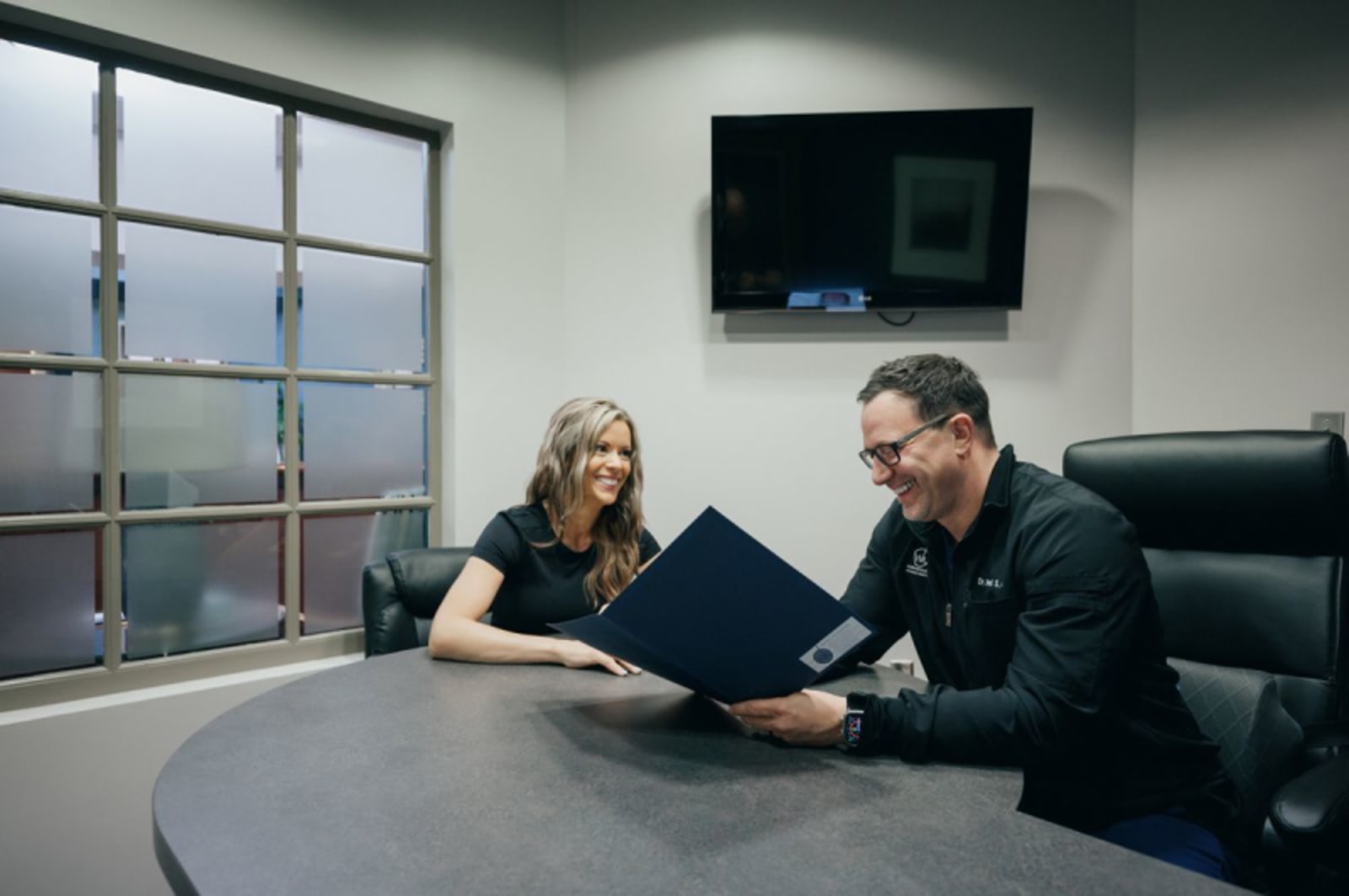 Two dental professionals reviewing treatment plan options at a consultation table in a modern office.