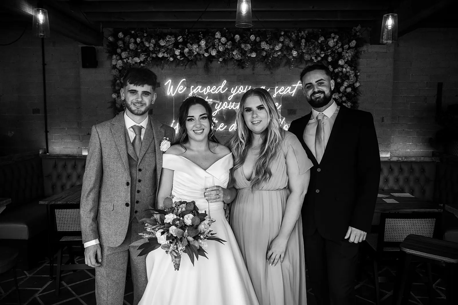 Wedding party in front of the flower wall and neon sign at Blackbrook Barns, Lichfield, Staffordshire