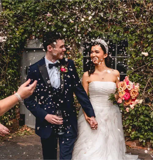 Newlyweds walking through confetti beside an ivy-covered wall at Blackbrook Barns, Lichfield, Staffordshire