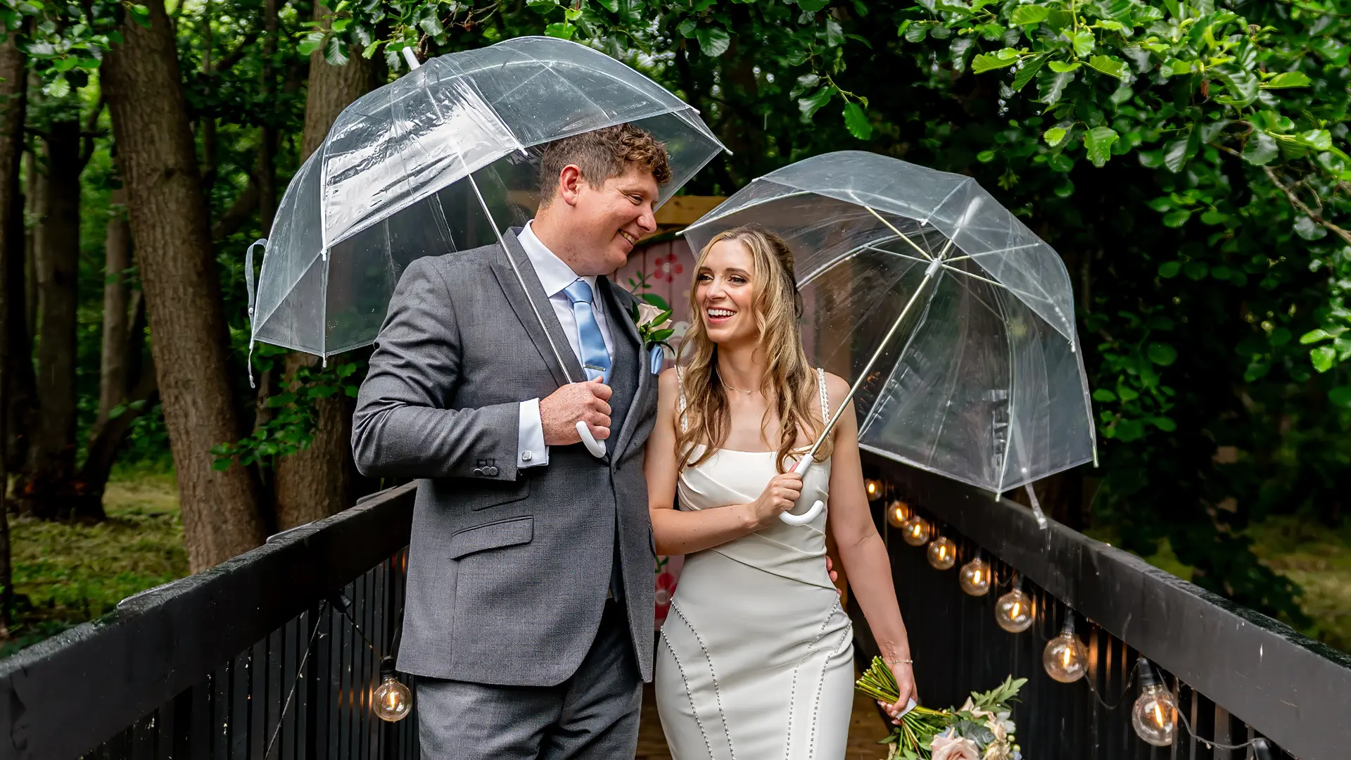Newlyweds with clear umbrellas on the bridge in the rain at Blackbrook Barns, Lichfield, Staffordshire