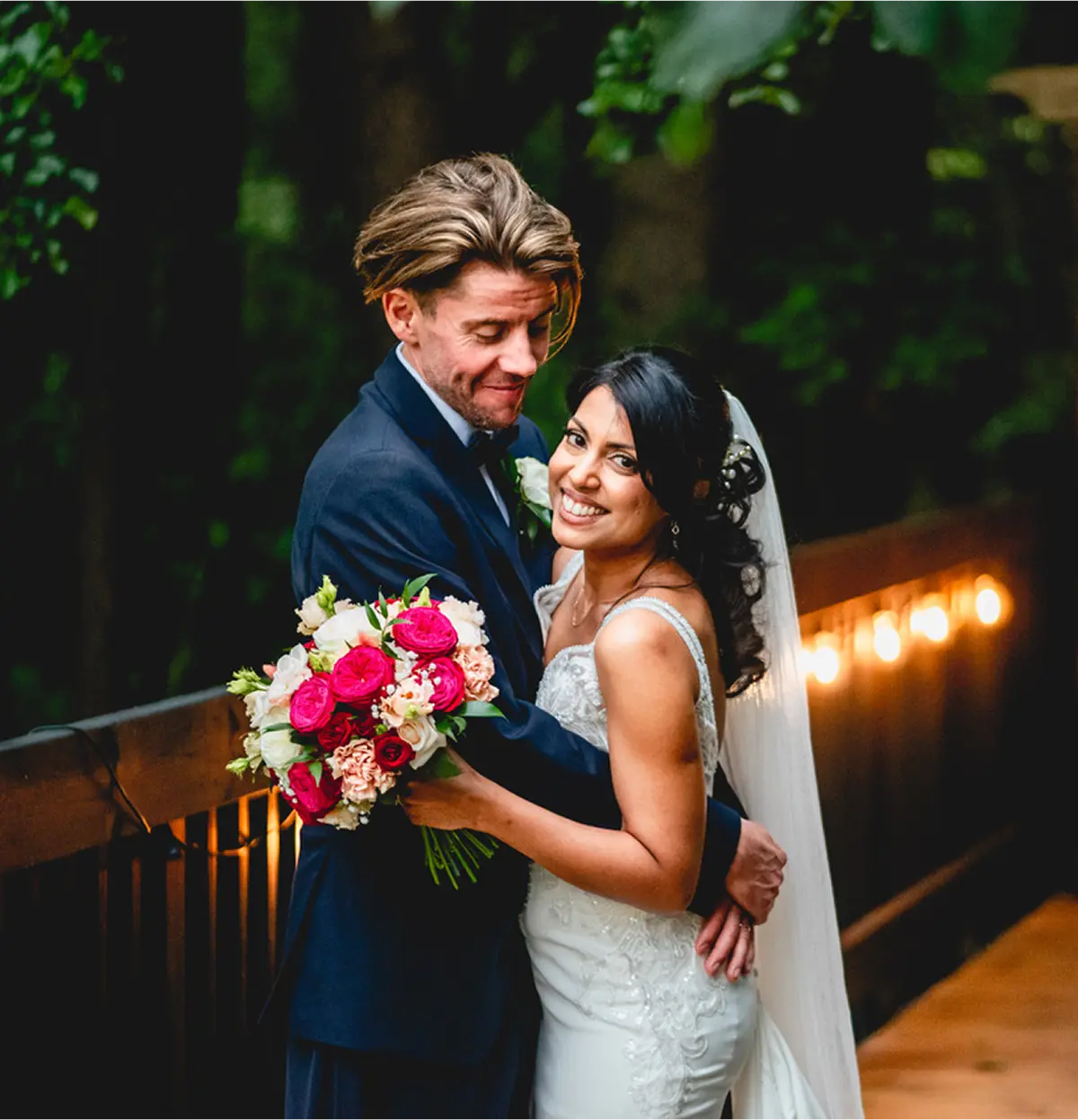 Newlyweds with a pink bouquet beneath festoon lights at Blackbrook Barns, Lichfield, Staffordshire