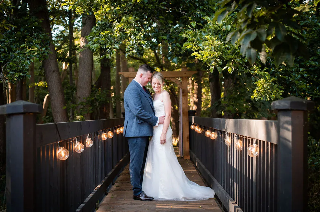 Newlyweds on the festoon-lit bridge at Blackbrook Barns, Lichfield, Staffordshire
