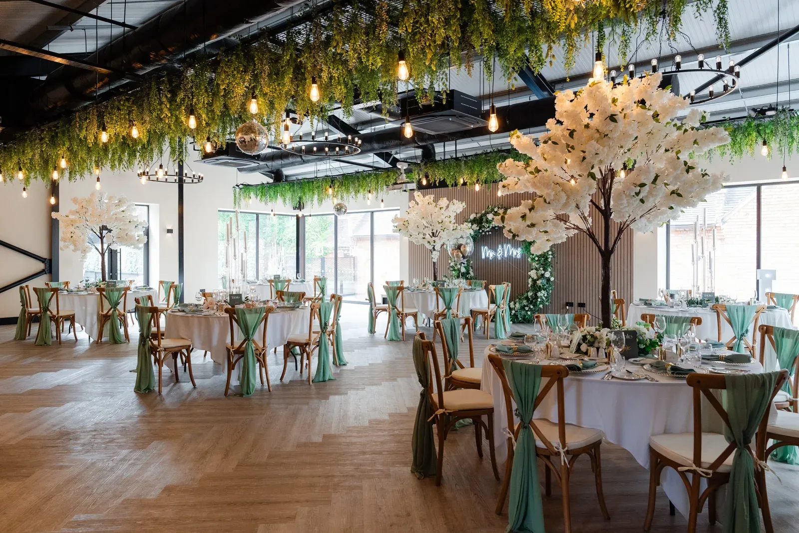 The Cow Shed set for a wedding reception with round tables and a blossom tree at Blackbrook Barns, Lichfield, Staffordshire