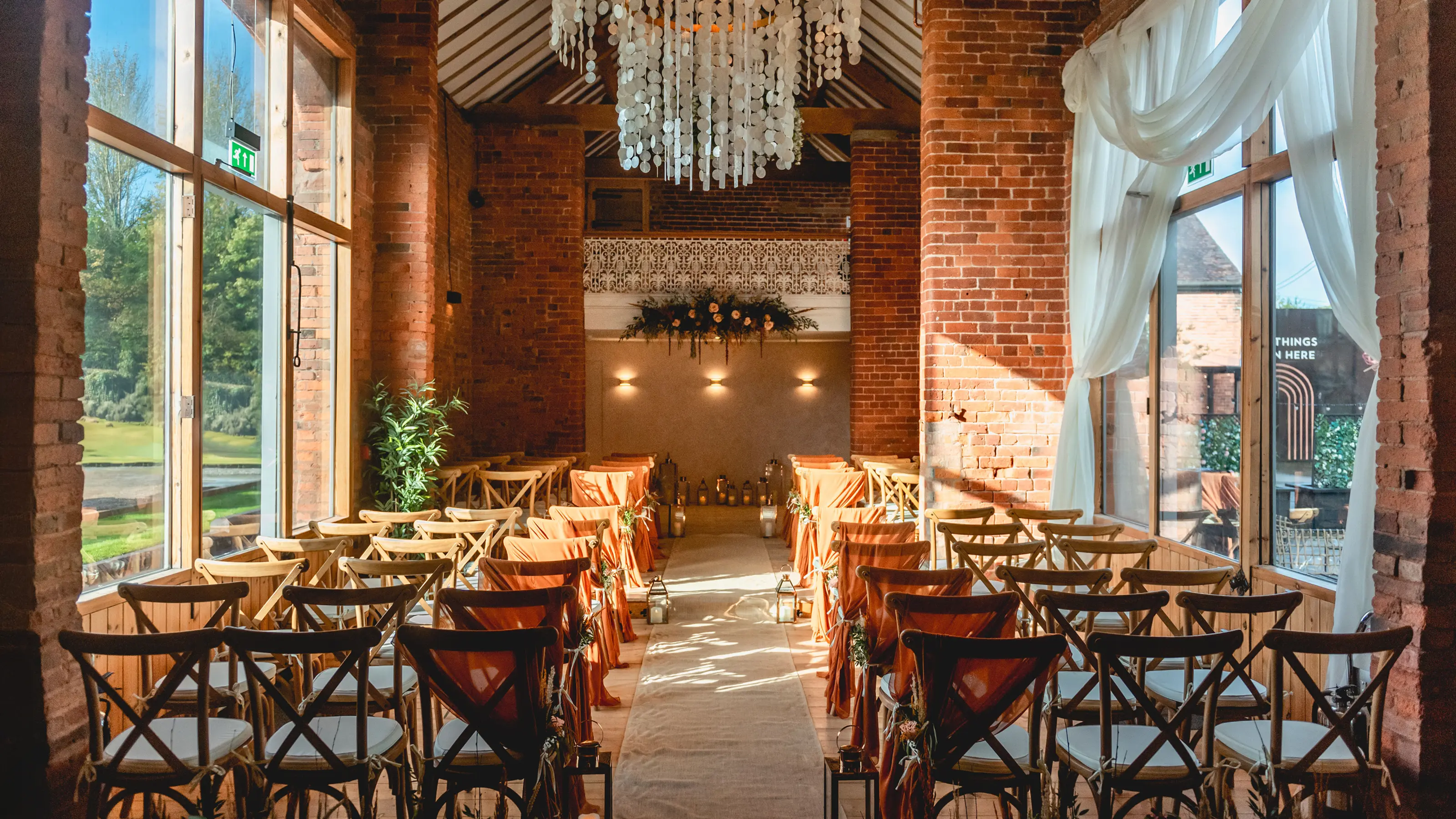 The Long Barn set for a ceremony with chandelier and exposed brick at Blackbrook Barns, Lichfield, Staffordshire