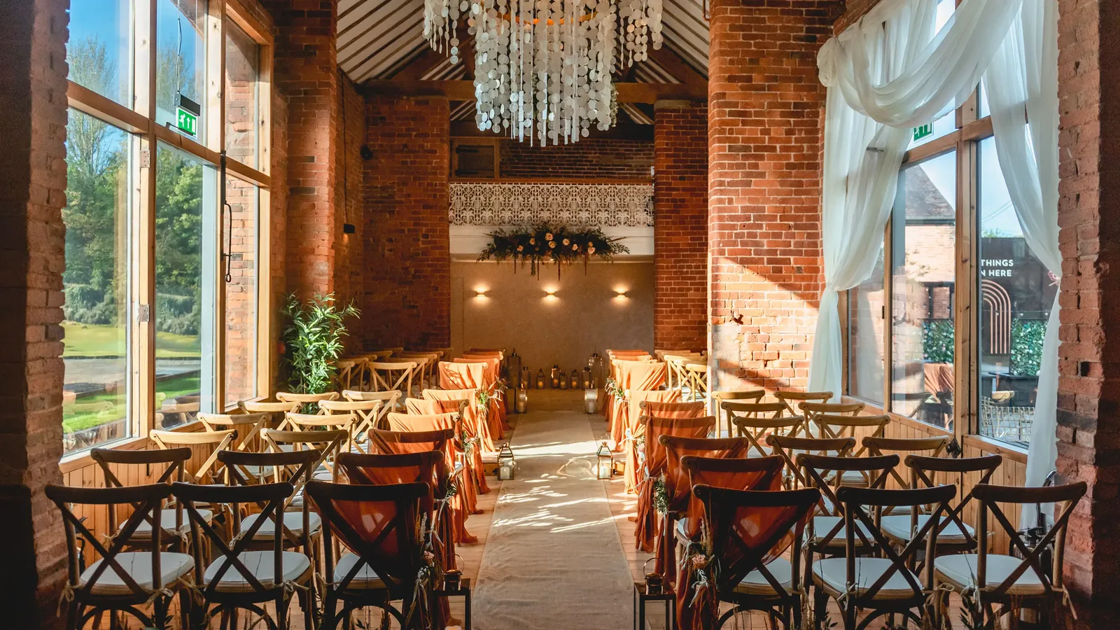 The Long Barn set for a ceremony with chandelier and exposed brick at Blackbrook Barns, Lichfield, Staffordshire