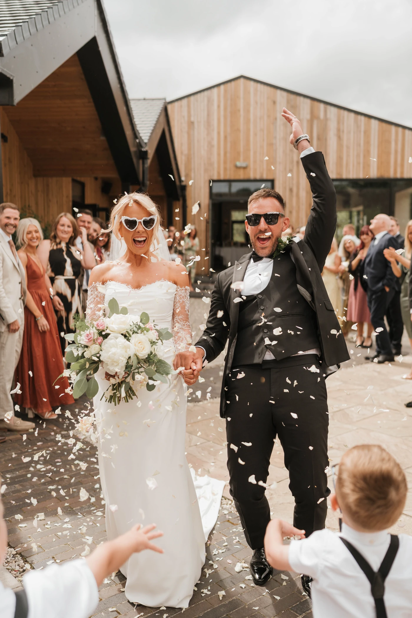 Newlyweds walking through a shower of petal confetti outside the barns at Blackbrook Barns, Lichfield, Staffordshire