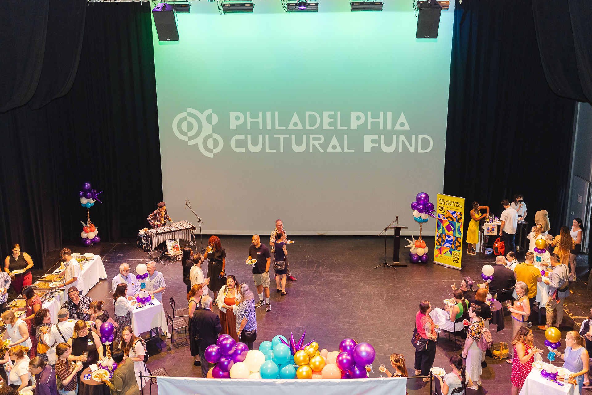 A photo of a party in a theater. People mill about on the stage. 