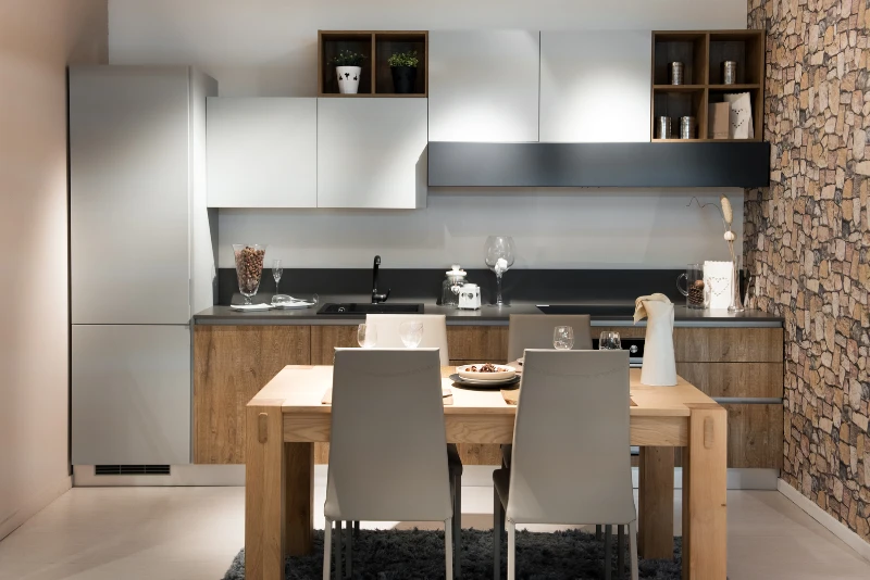 Loft studio with front dormer, kitchenette with open shelves, compact sofa, sloped ceiling, and neutral decor.