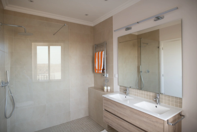 Rear dormer en‑suite with skylight window, walk-in shower with glass screen, wall-mounted toilet and basin, white tiles, and built-in alcove shelves.