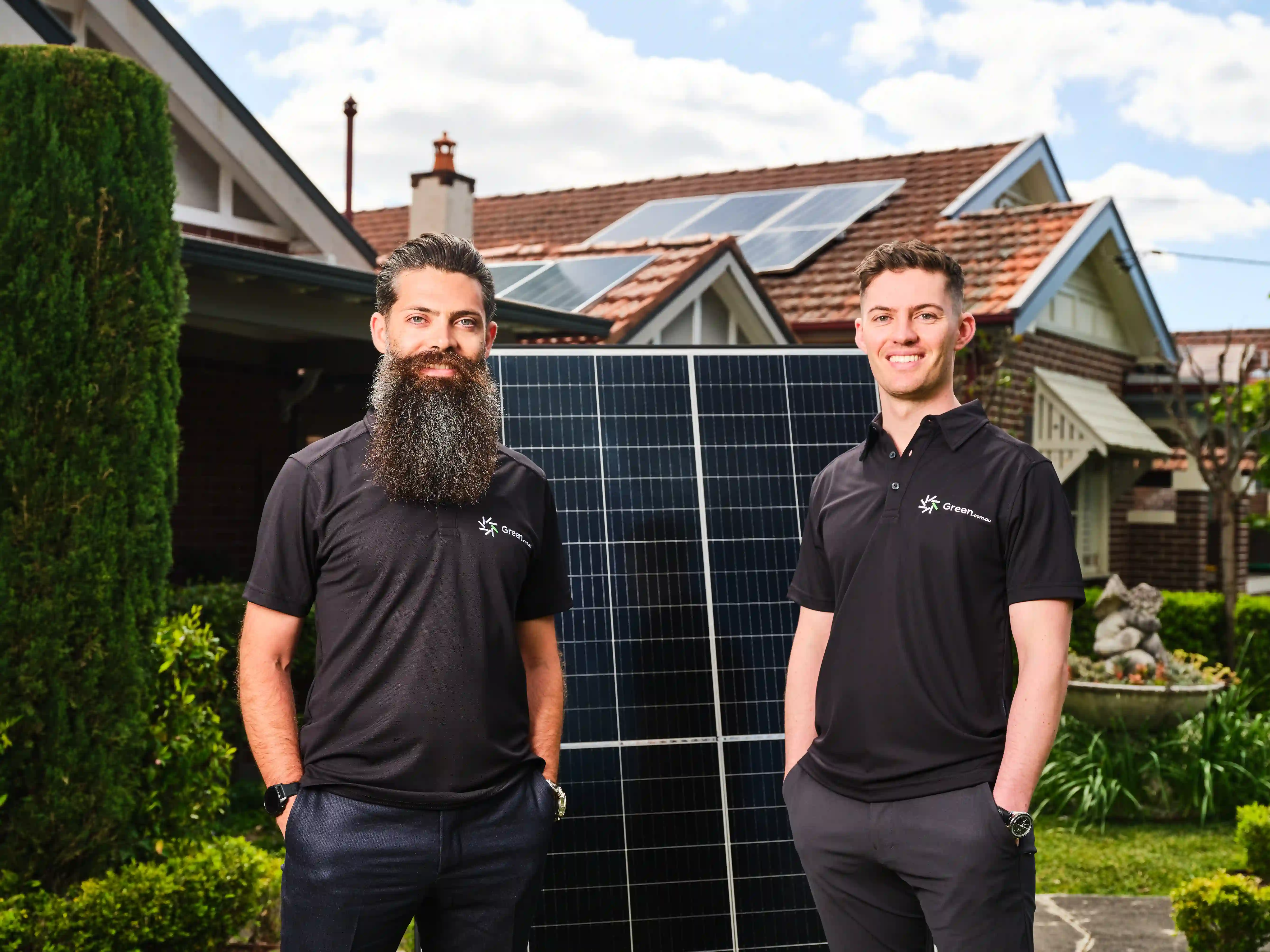 Founders, David & Jono Green, standing in a residential home's front garden with a large solar panel.