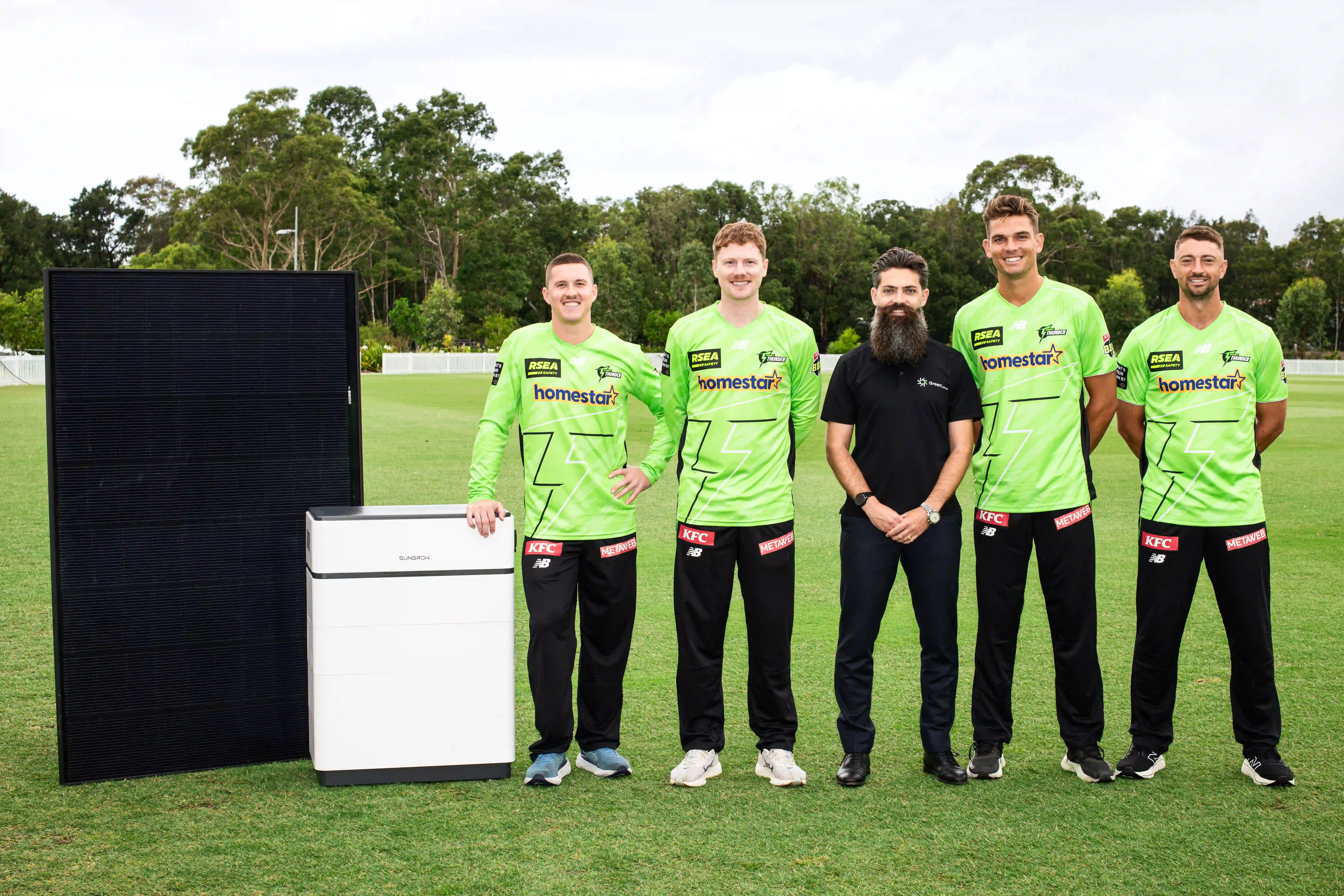 David Green and players from Sydney Thunder cricket team standing alongside a battery and solar panel on the cricket pitch.