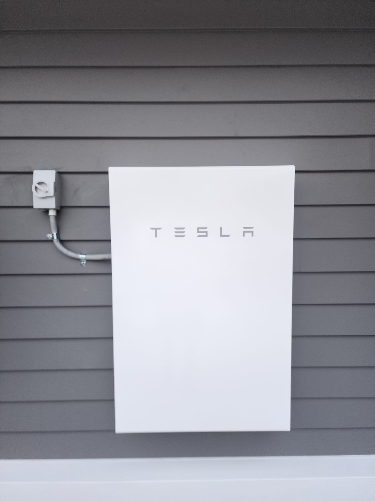 Tesla Powerwall installed on a grey wall.