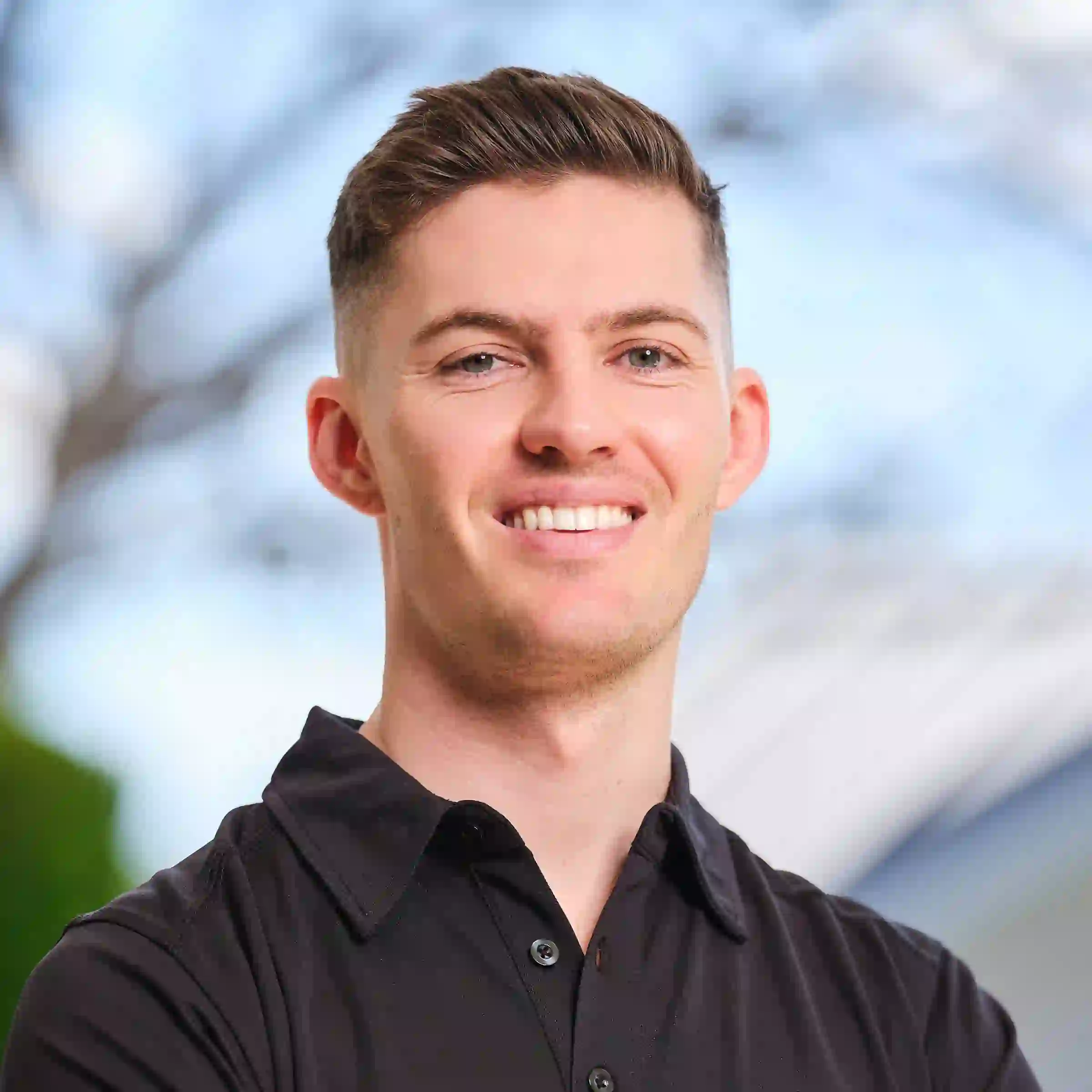Jonathan Green in a Green.com.au polo shirt standing against a background of sky and trees