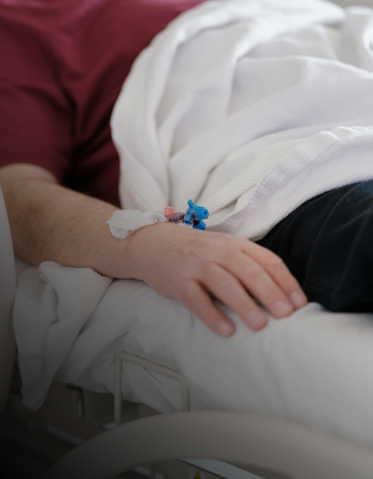 Close-up of a patient's hand with an intravenous line inserted, resting on a hospital bed.