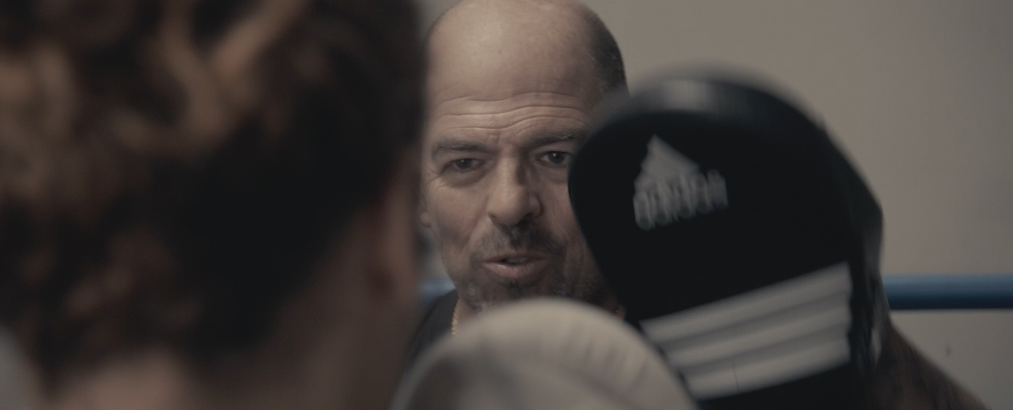 Un entraîneur concentré regarde un boxeur portant des gants de boxe Adidas pendant l'entraînement.