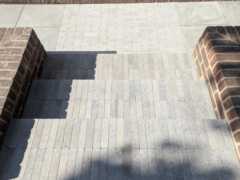 Stone steps with light gray rectangular tiles bordered by brown brick walls on each side.