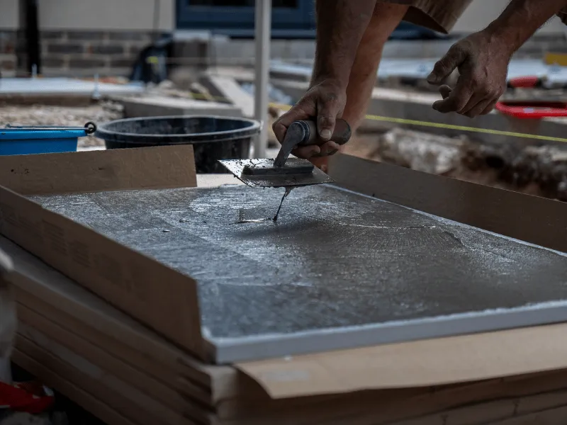 Worker applying wet concrete with a trowel on a flat surface outdoors.
