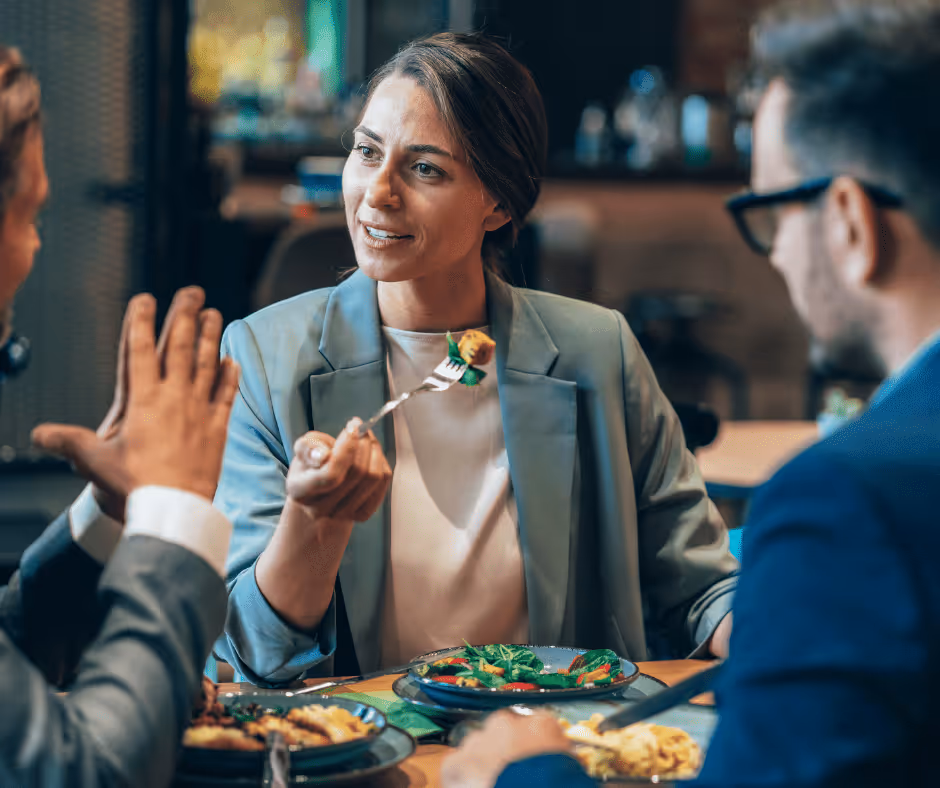 Three professionals having a discussion while eating a meal at a restaurant table.