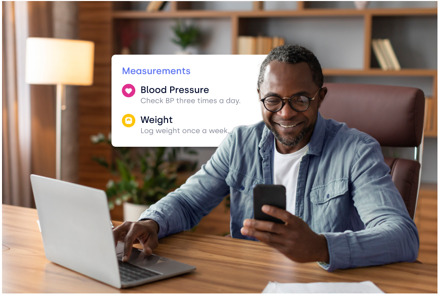 Smiling man sitting at desk with laptop and smartphone, with overlay showing health measurements for blood pressure and weight.