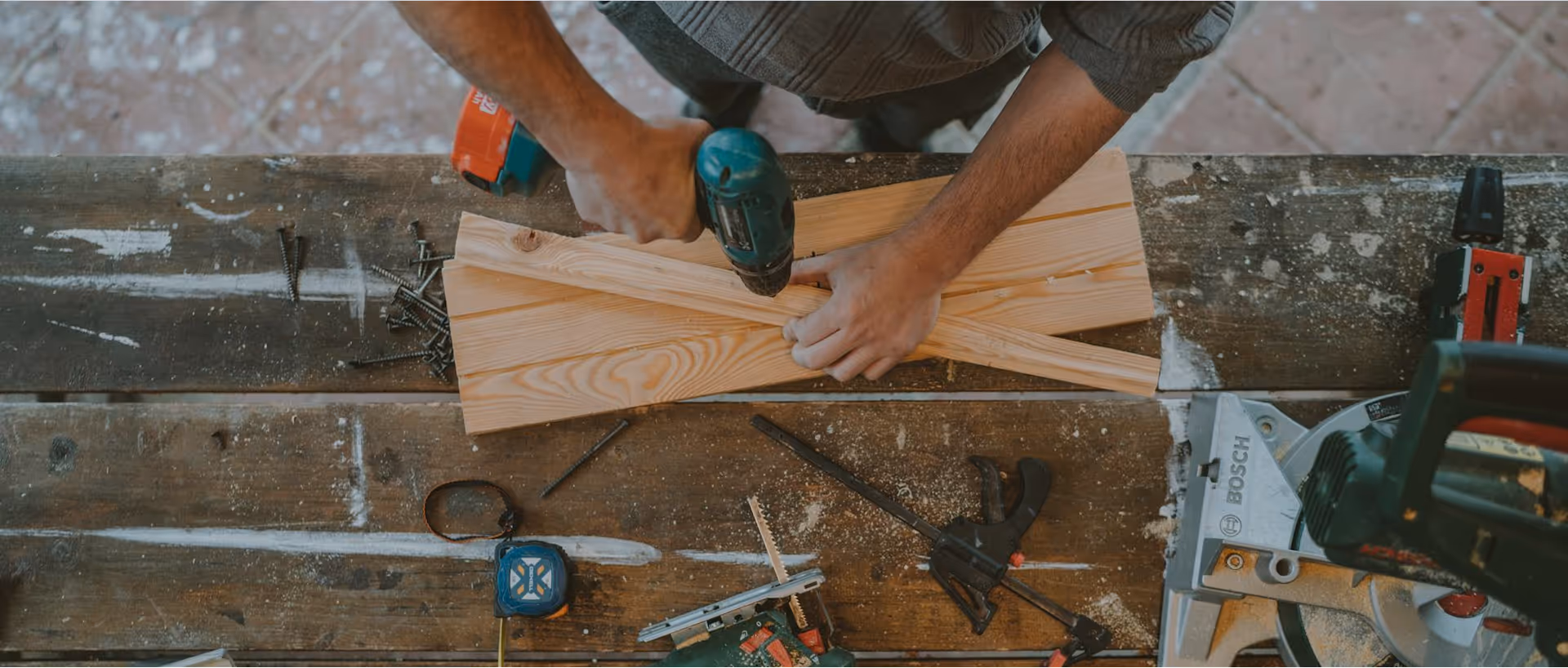 Handwerker bohrt Schraube in zwei Holzstücke auf einer Werkbank mit Werkzeugen.
