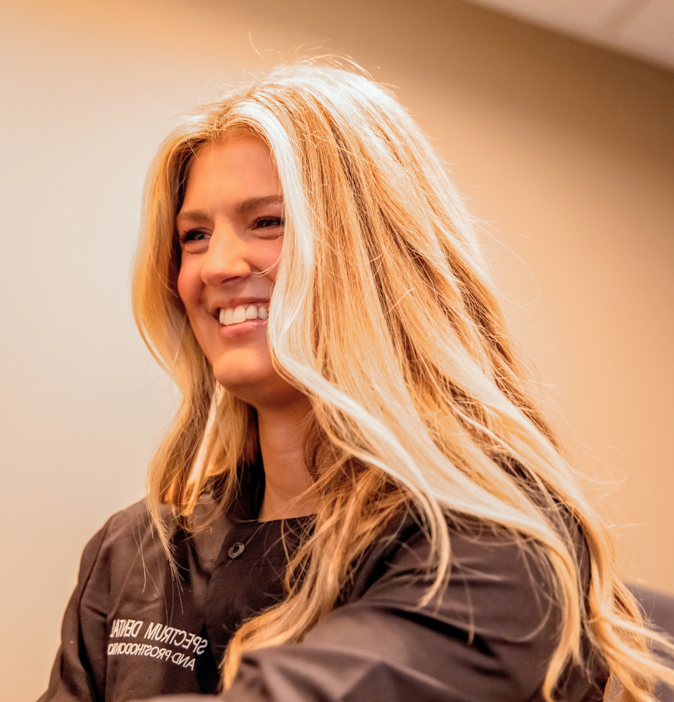 A woman with long, wavy blonde hair wears a black professional jacket, showcasing a warm and inviting atmosphere.