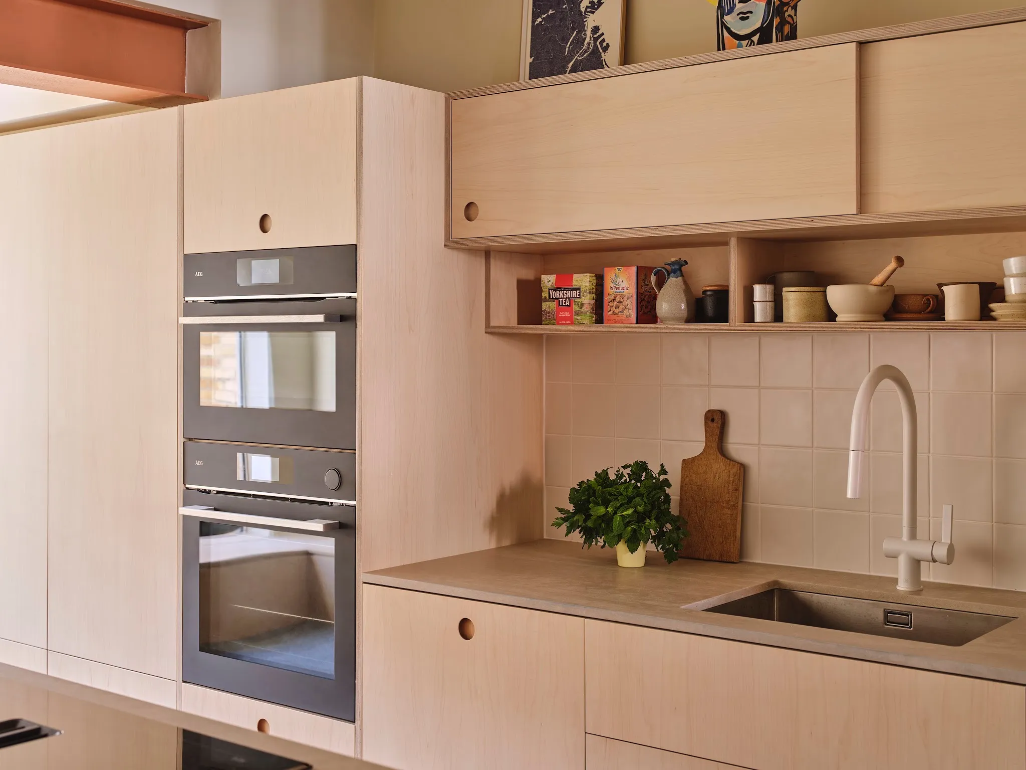 Birch plywood Core kitchen by Uncommon with integrated AEG ovens, open shelving and tiled splashback in Edd Kimber’s home.