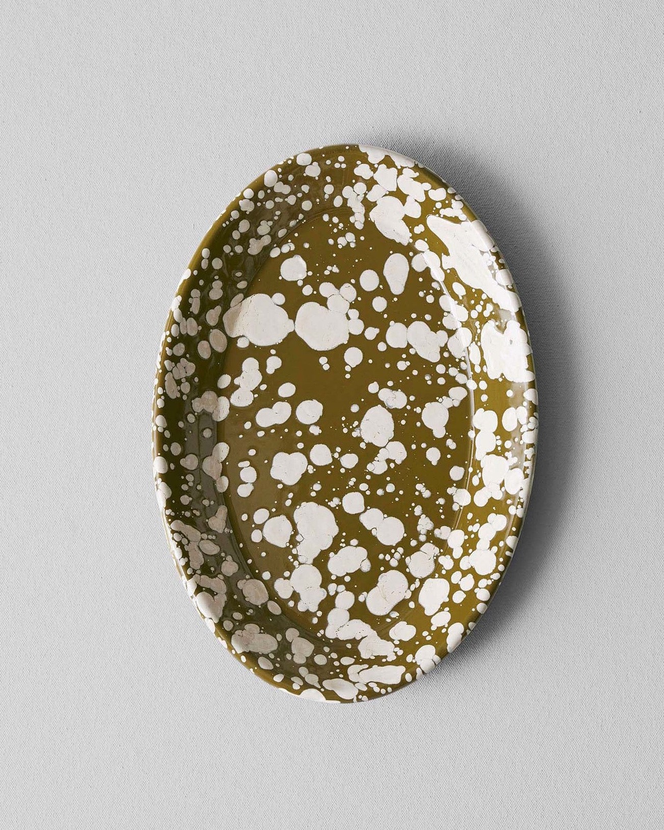 Olive green enamel splatterware platter with white pattern on a grey background.