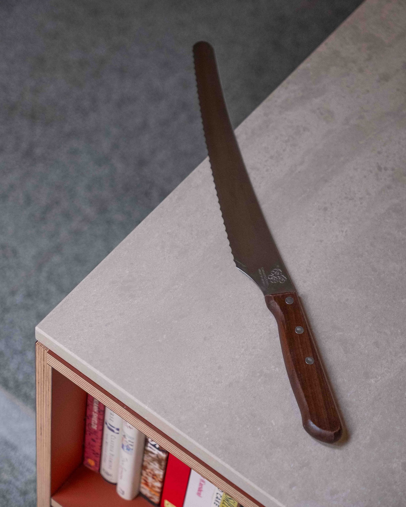 Japanese serrated bread knife with dark wooden handle placed on a plywood kitchen worktop.