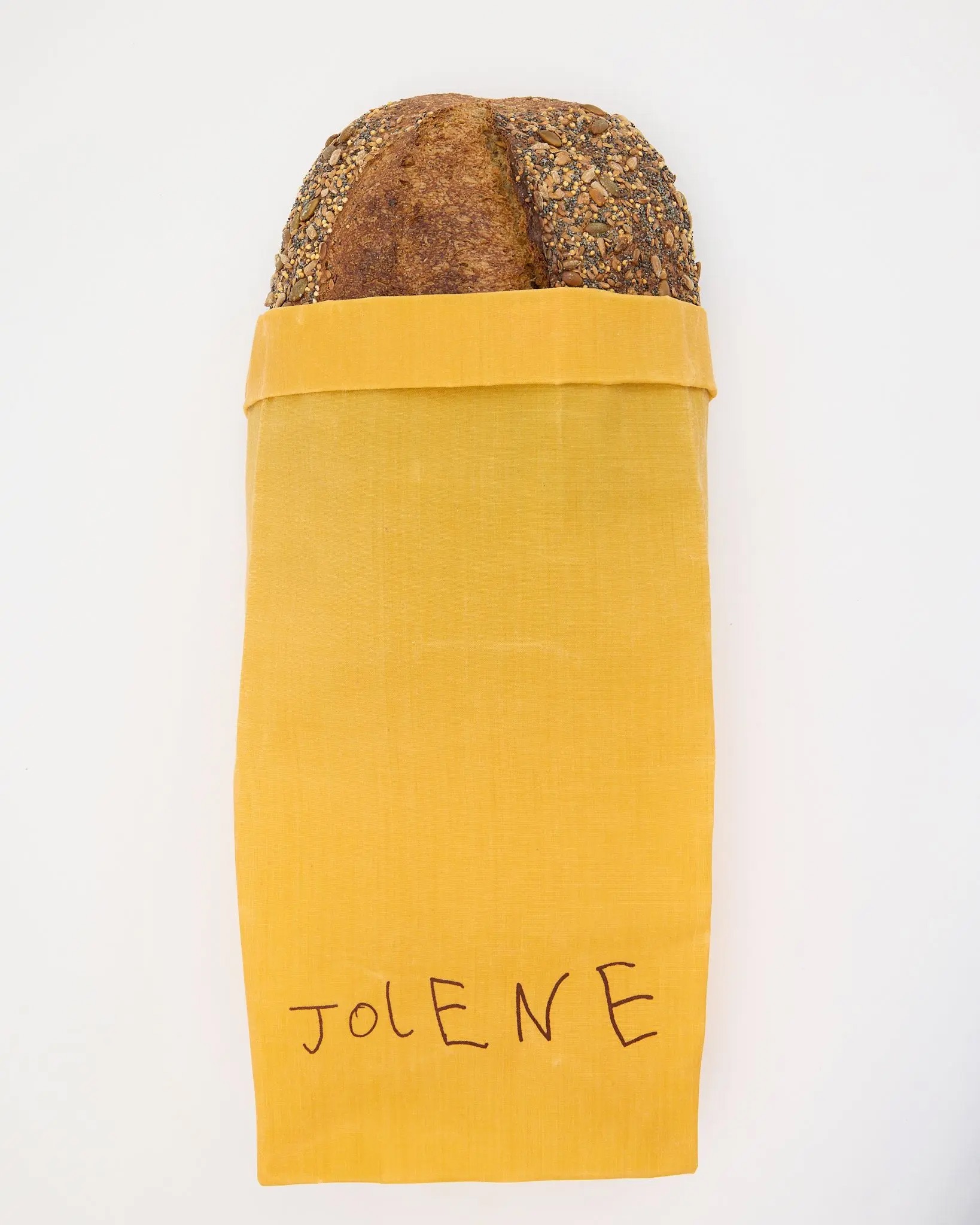 Yellow beeswax bread bag from Jolene Bakery holding a loaf of sourdough bread.