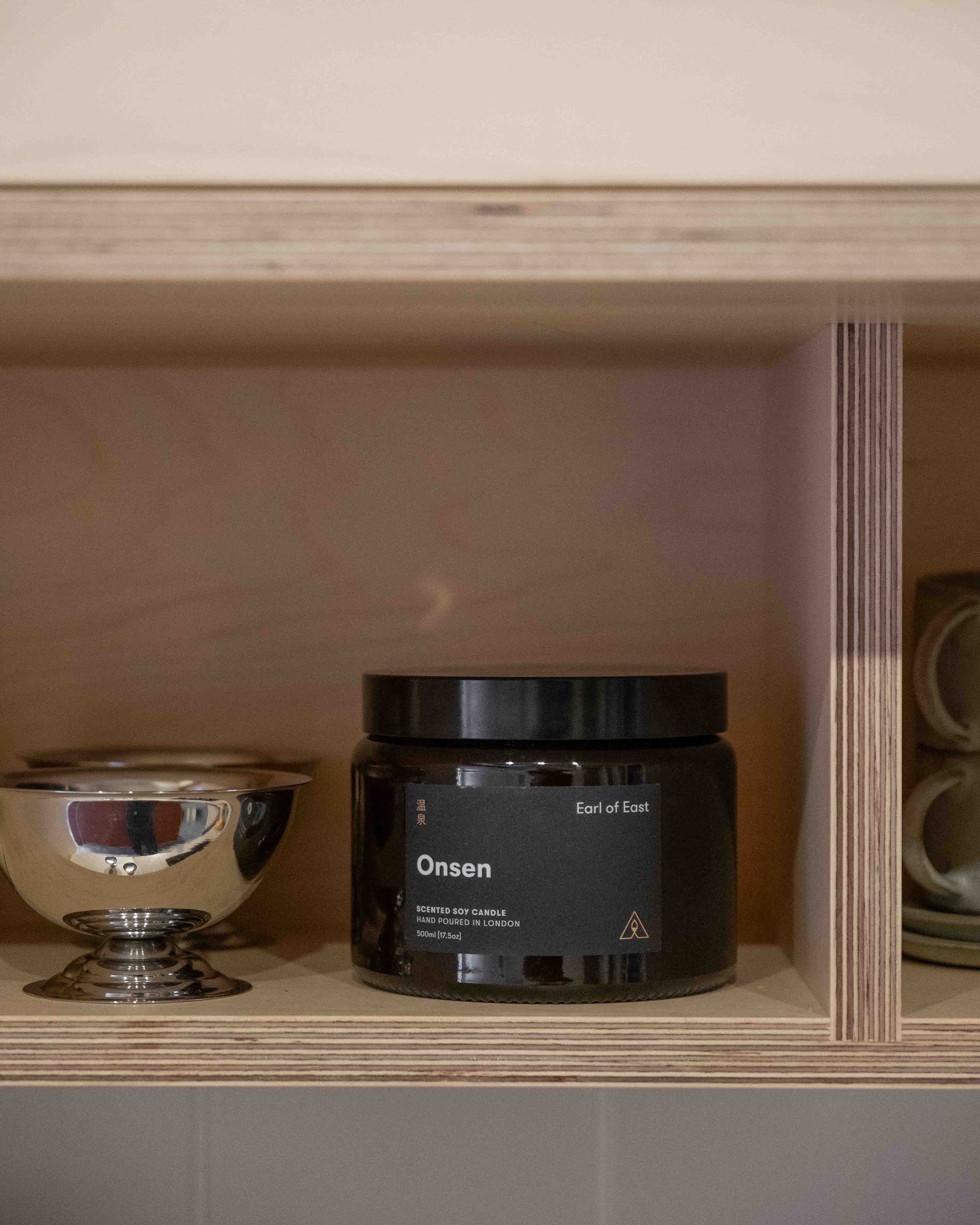 Earl of East Onsen scented candle displayed on plywood shelving in an Uncommon kitchen.